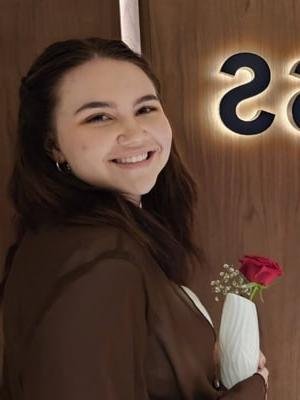 Image of Lacy M wearing a brown sweater and holding a flower vase with a red rose. 